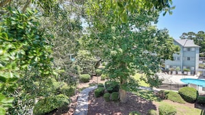 A pool area with a curved pathway, surrounded by well-maintained bushes and trees, and a building with a light blue exterior in the background. - Swim, Soak + Play: Myrtle Beach Resort Condo! (Myrtle Beach)