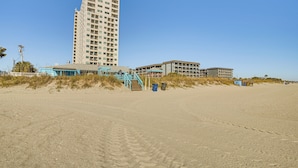 A beachfront hotel with a tall building, a staircase leading to the beach, and a sandy path. - Swim, Soak + Play: Myrtle Beach Resort Condo! (Myrtle Beach)