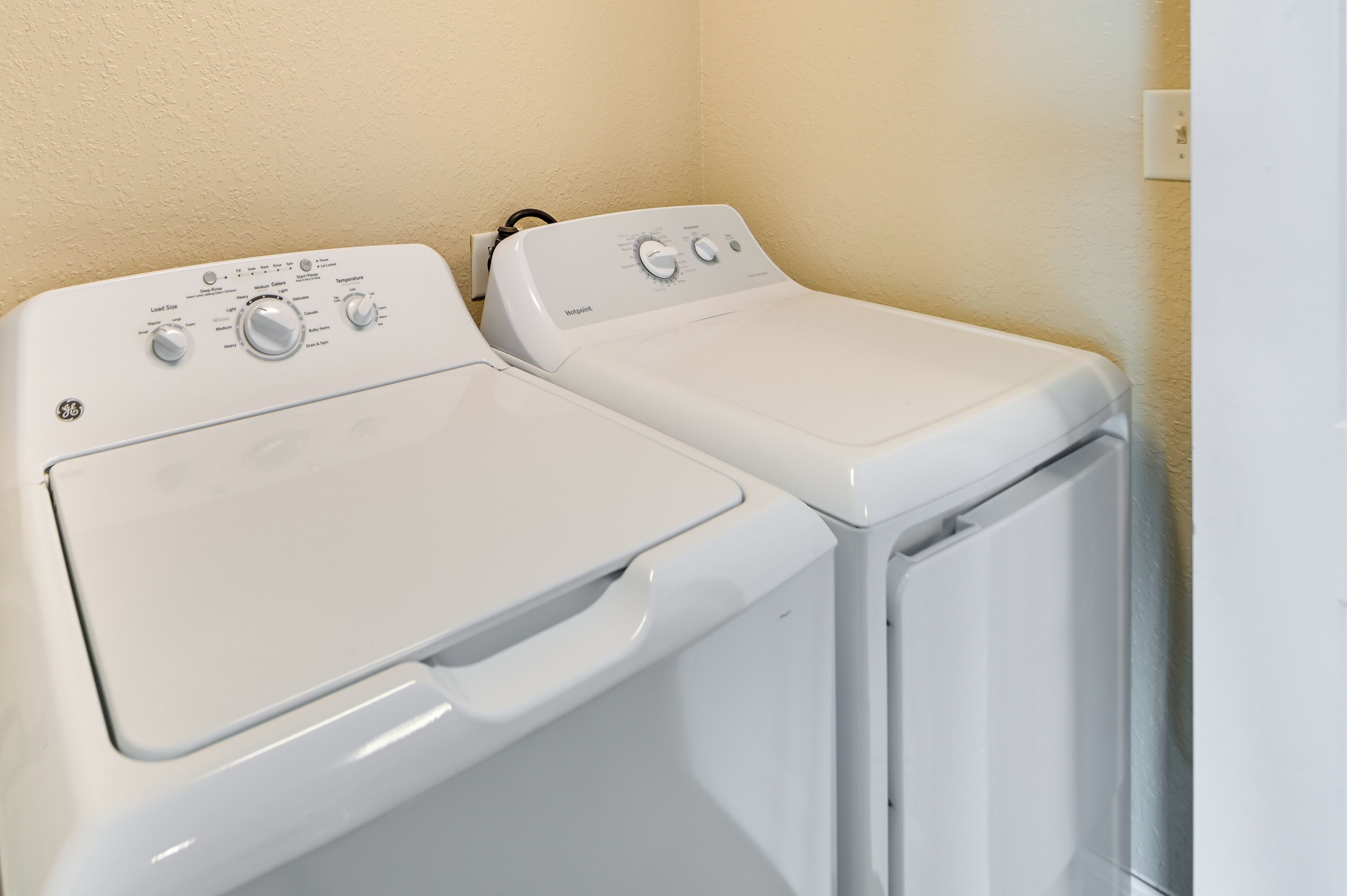 Two white front-loading washing machines in a laundry room with beige walls.