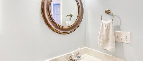 A bathroom with a round mirror, a sink, a towel rack, and a soap dispenser.