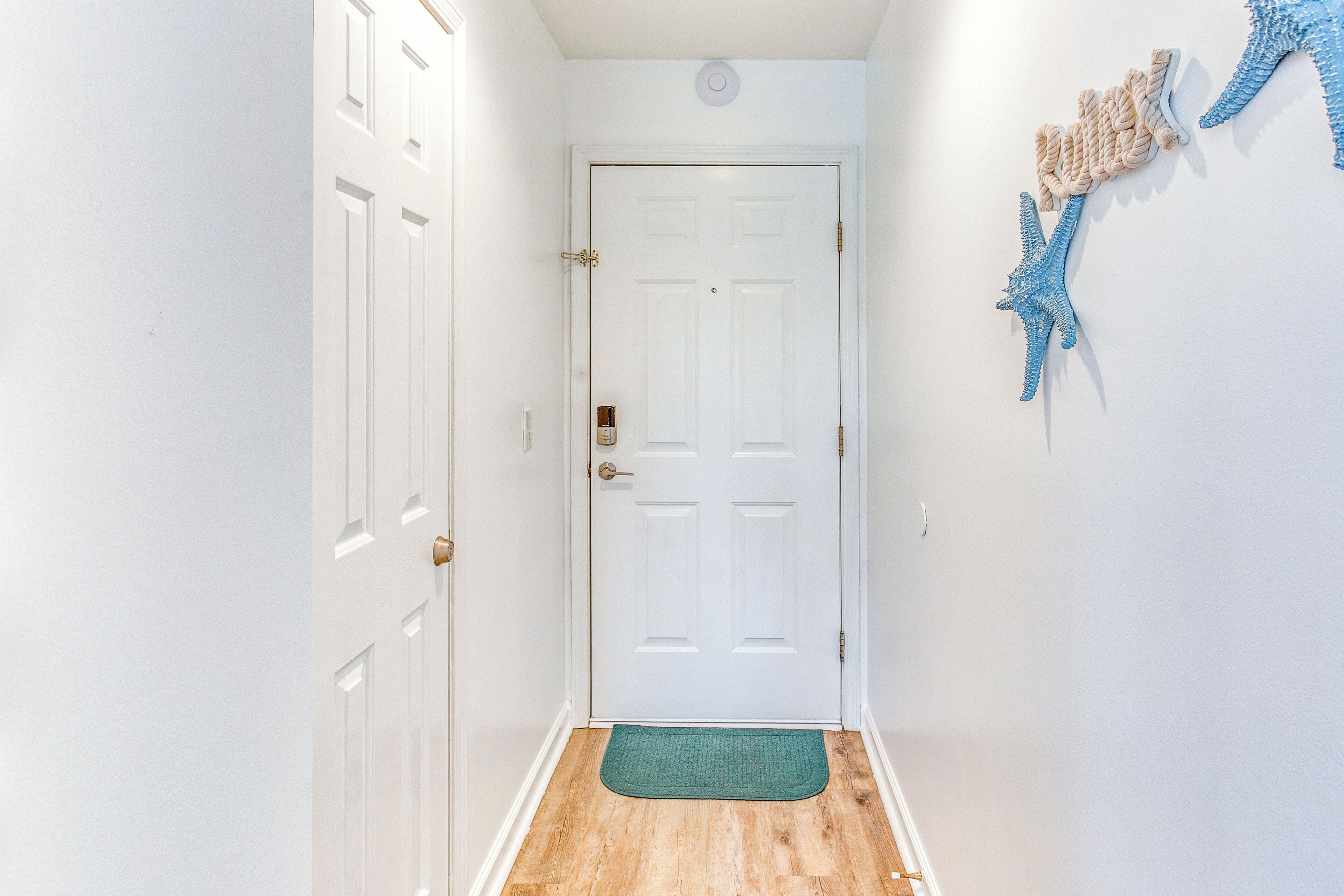 A hallway with a white door, a green doormat, and blue wall decorations.