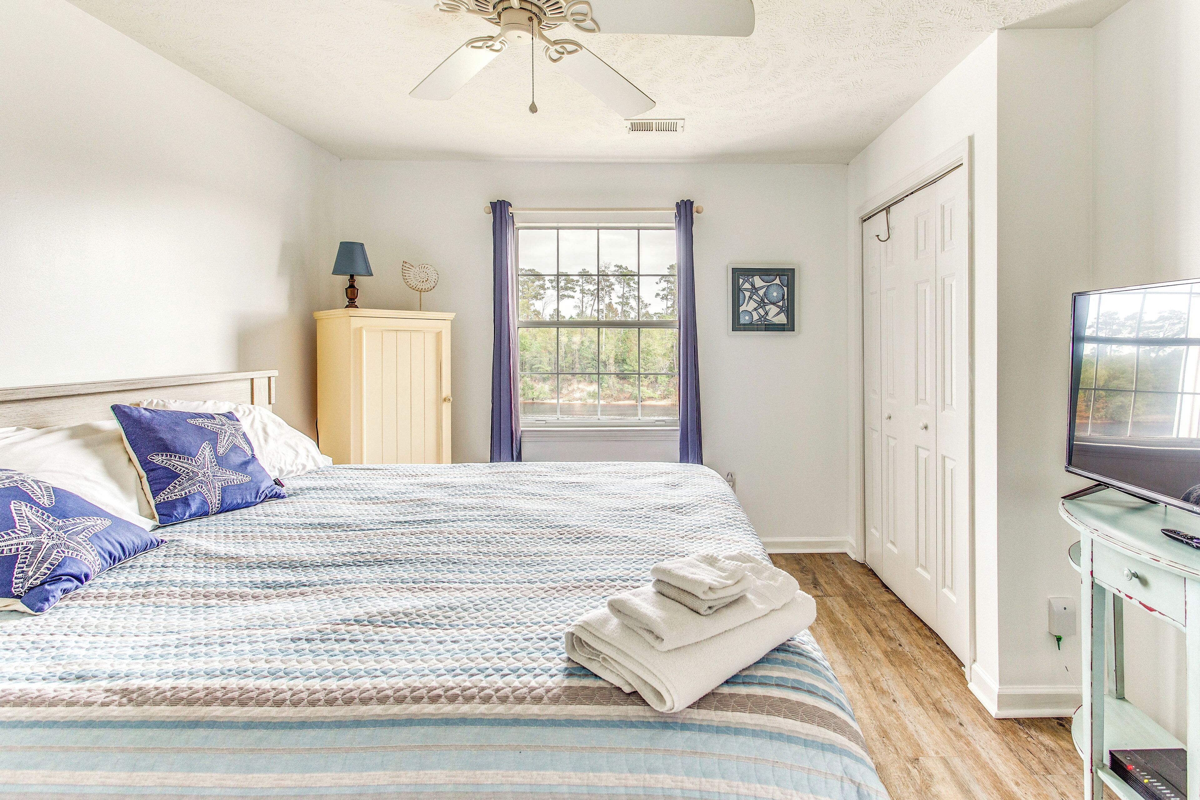 Un dormitorio con cama, televisión, armario y ventana con cortinas.
