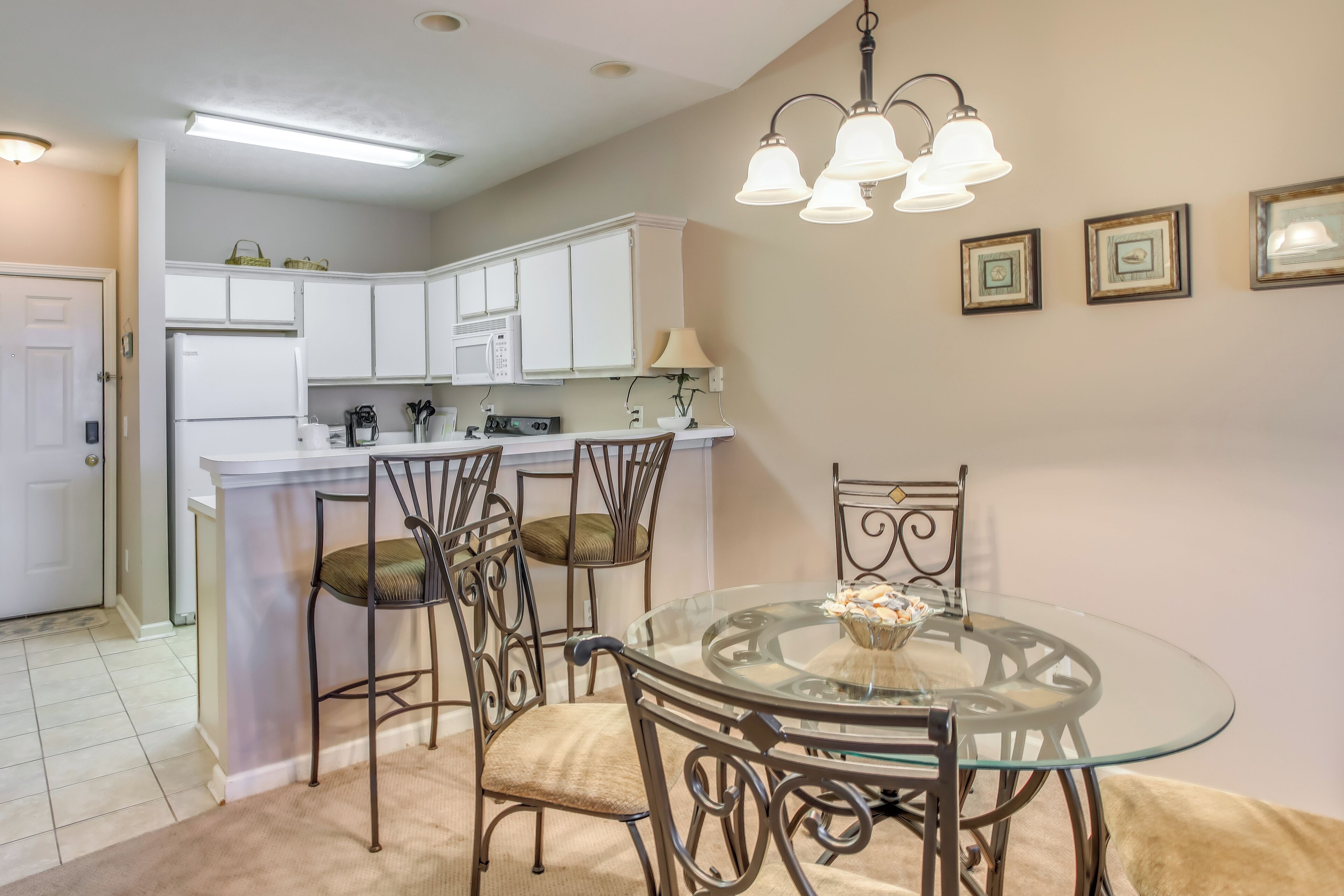 A compact kitchen with white cabinets, a central island, and a dining area with a glass table and metal chairs.