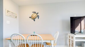 Ein Essbereich mit Holztisch und weißen Stühlen, einer an der Wand befestigten Schildkröten-Dekoration und einem Fernseher auf einem weißen Schrank.