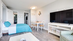 Ein modernes, gut beleuchtetes Zimmer mit einem Bett, einem Esstisch mit Stühlen, einem Fernseher und einer kleinen Schreibtischzeile.