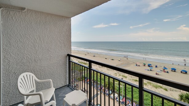 A balcony with a view of a beach, white chairs, and umbrellas. - Oceanfront Studio w/ Pool Access in Myrtle Beach! (Myrtle Beach)