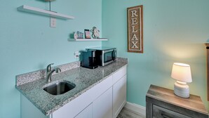A kitchen with a granite countertop, stainless steel sink, and a microwave. There is a shelf with decorative items and a 'RELAX' sign on the wall. - Oceanfront Studio w/ Pool Access in Myrtle Beach! (Myrtle Beach)