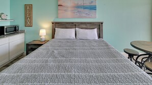 A bedroom with a bed, a nightstand with a lamp, a microwave, a small table, and a painting on the wall. - Oceanfront Studio w/ Pool Access in Myrtle Beach! (Myrtle Beach)