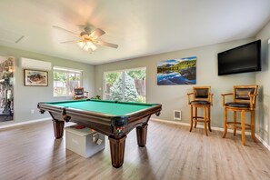 A pool table in a room with wooden flooring, a ceiling fan, and two bar stools.