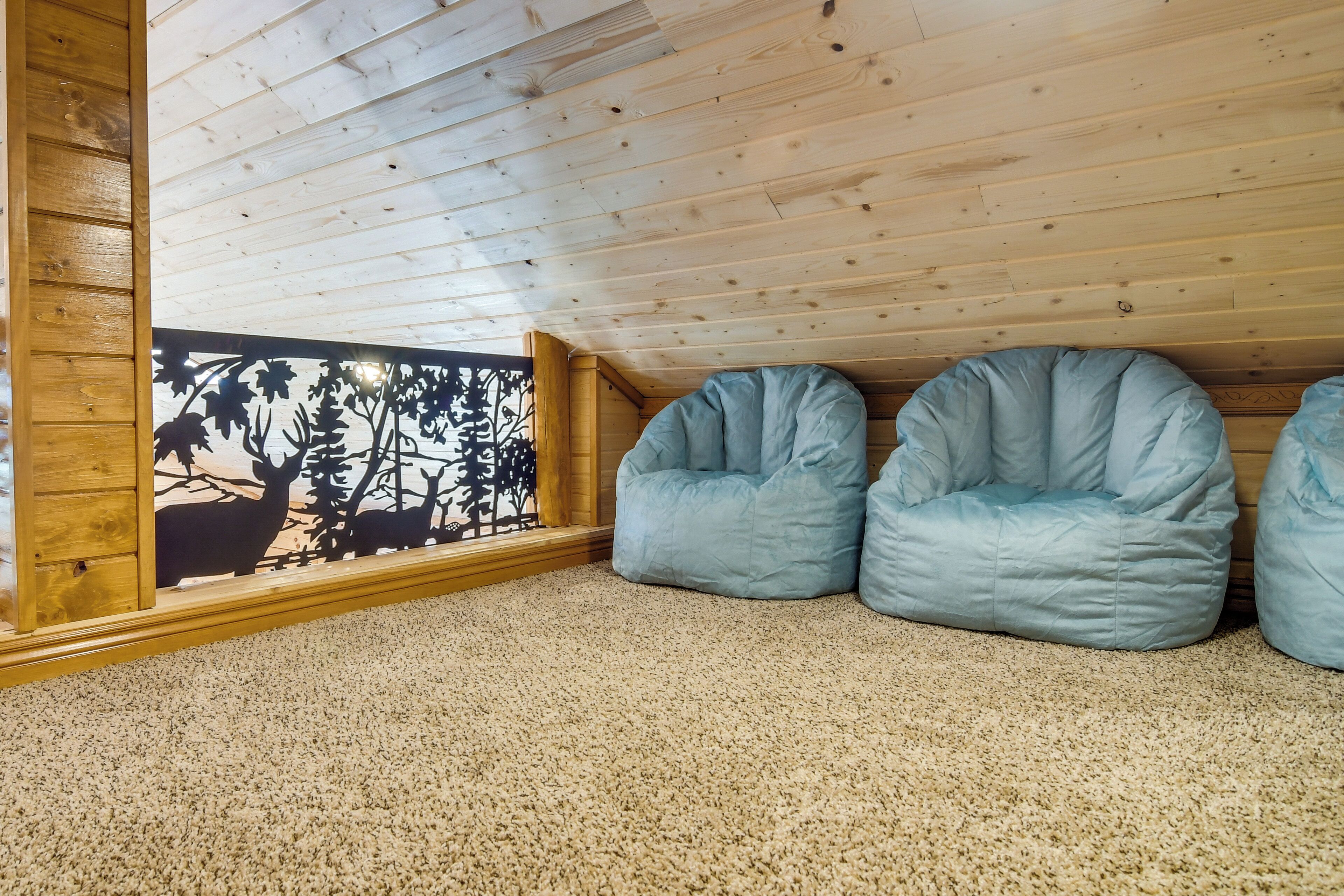 A cozy attic room with a sloped ceiling, two blue bean bags, a wooden floor, and a decorative window with a forest scene.