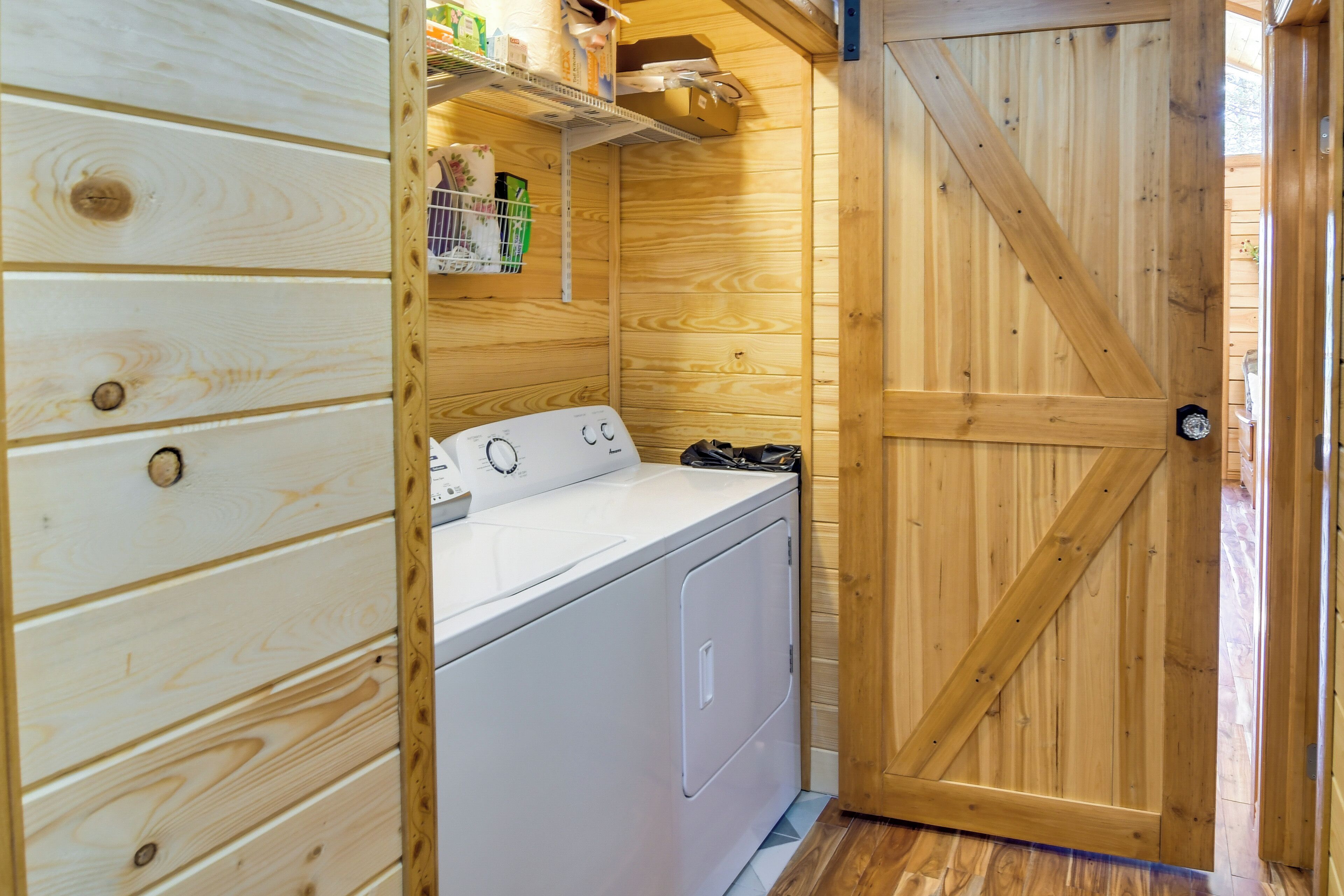 A laundry room with a white washer and dryer, wooden walls, and a wooden door.