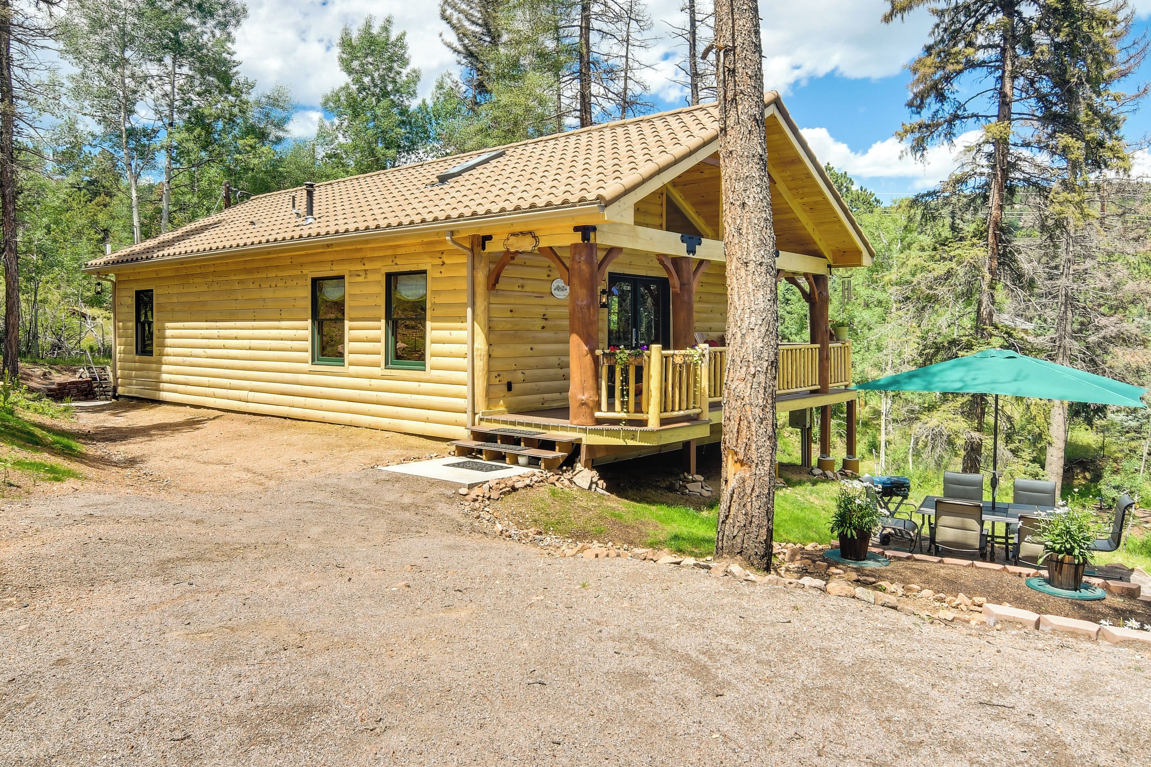 A log cabin with a porch, a covered outdoor seating area, and a dirt driveway.