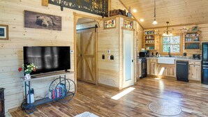 Interior de una cabaña de madera con televisión, pisos de madera, chimenea y una zona de cocina.