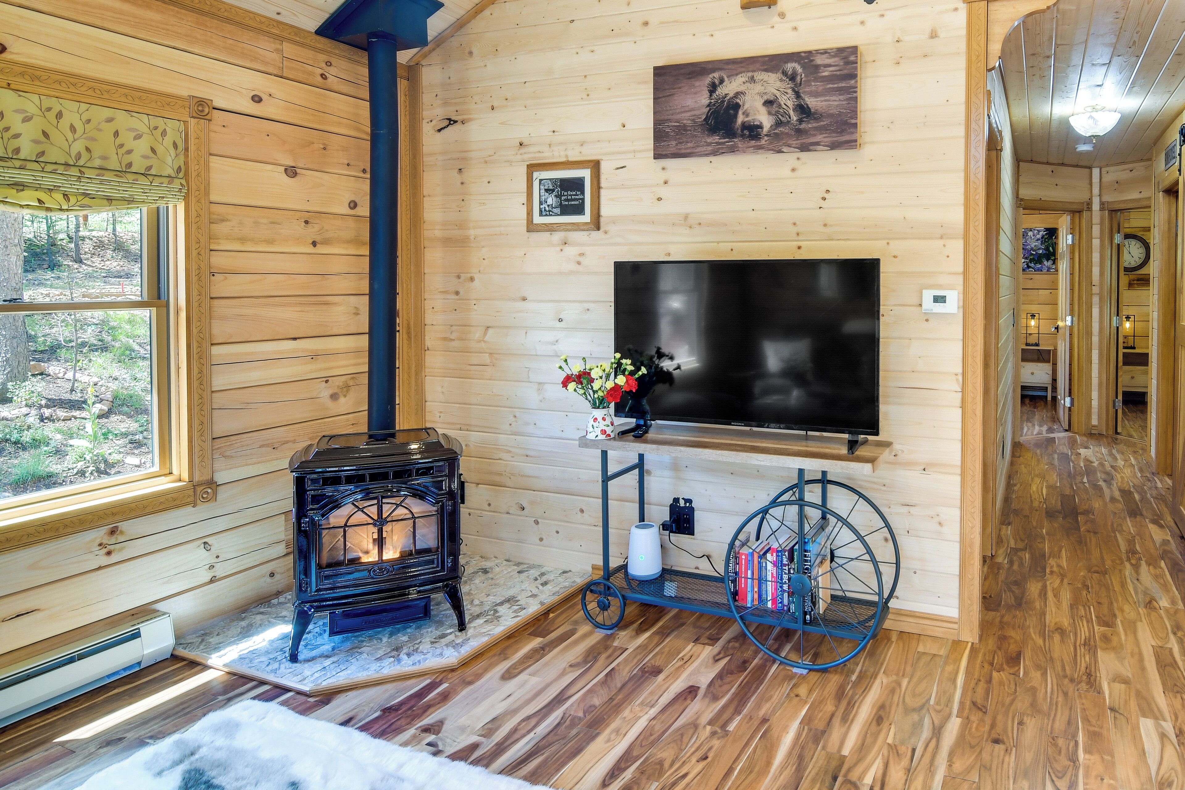 Un interior de cabaña acogedor con estufa de leña, televisor montado y estantería.