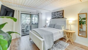 Une chambre à coucher comprenant un lit, des tables de chevet, un grand miroir et une porte-fenêtre coulissante donnant sur un balcon.