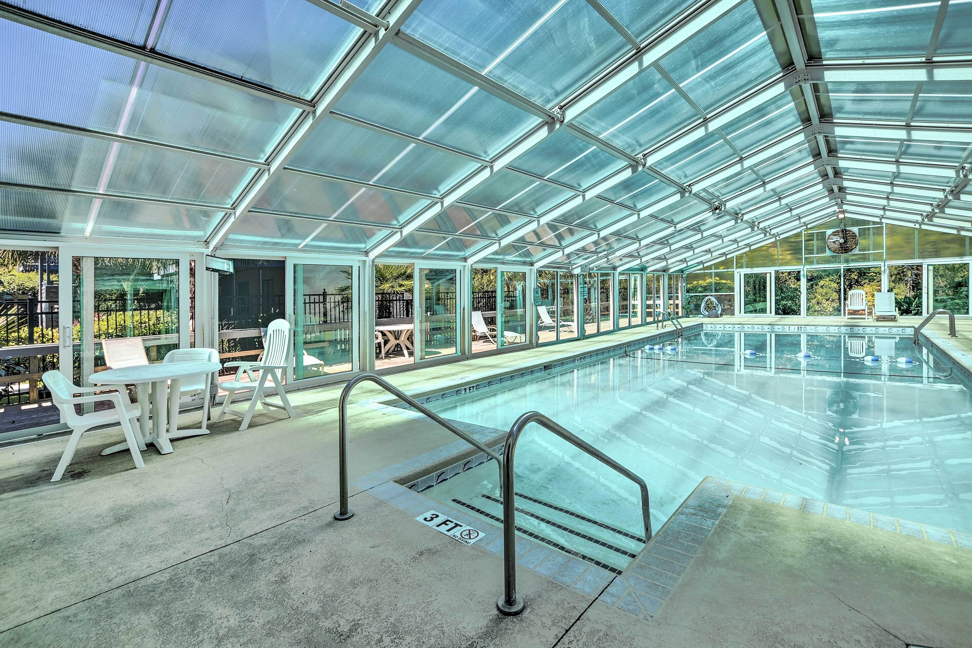 Una piscina techada con paredes de vidrio, barandillas metálicas y algunas sillas y mesas.