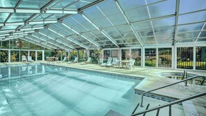 Une grande piscine intérieure dotée d’un toit en verre transparent, de chaises longues et d’un petit espace avec des tables.
