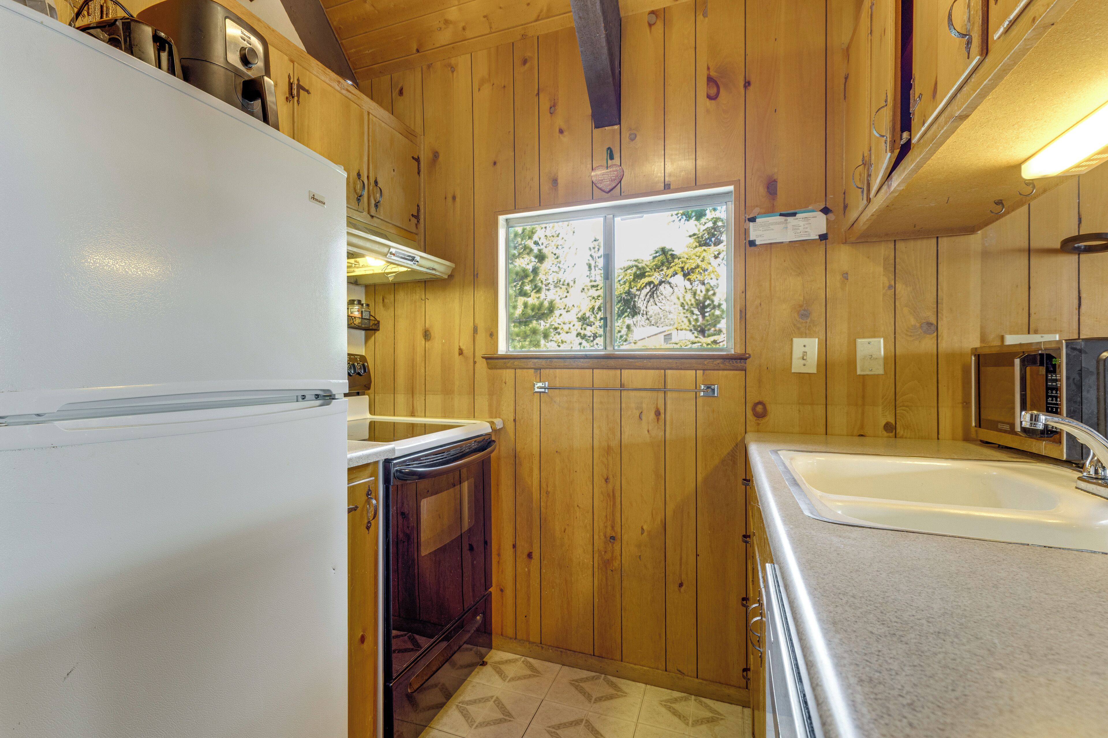 A compact kitchen with wooden walls, a white refrigerator, a sink, and a window with a view.
