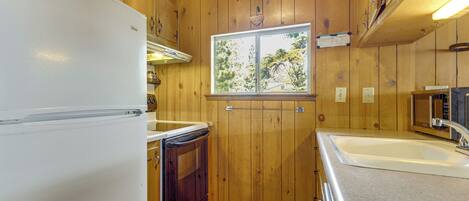 A compact kitchen with wooden walls, a white refrigerator, a sink, and a window with a view.