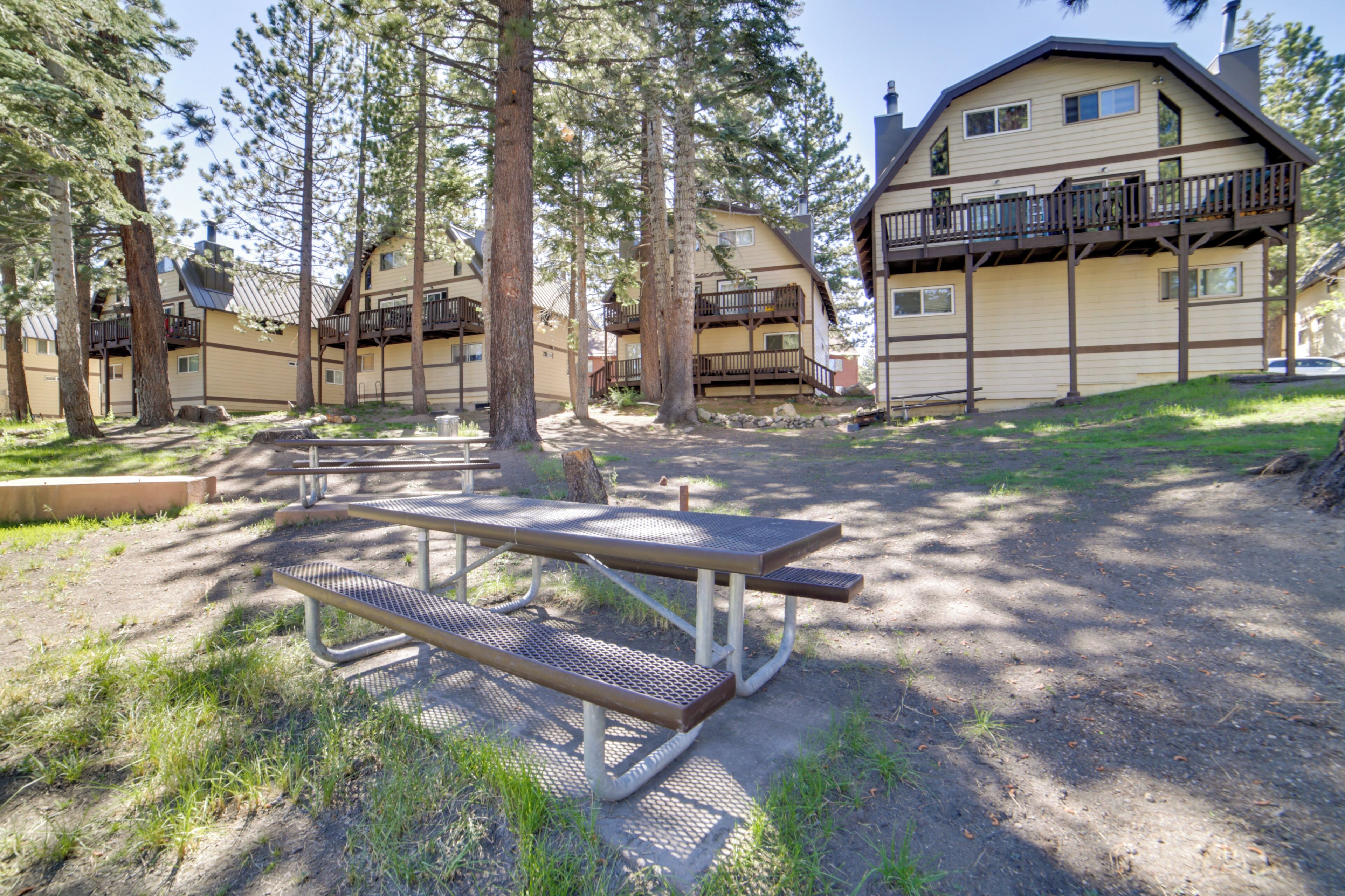 A campground with picnic tables, a large building with balconies, and surrounding trees.