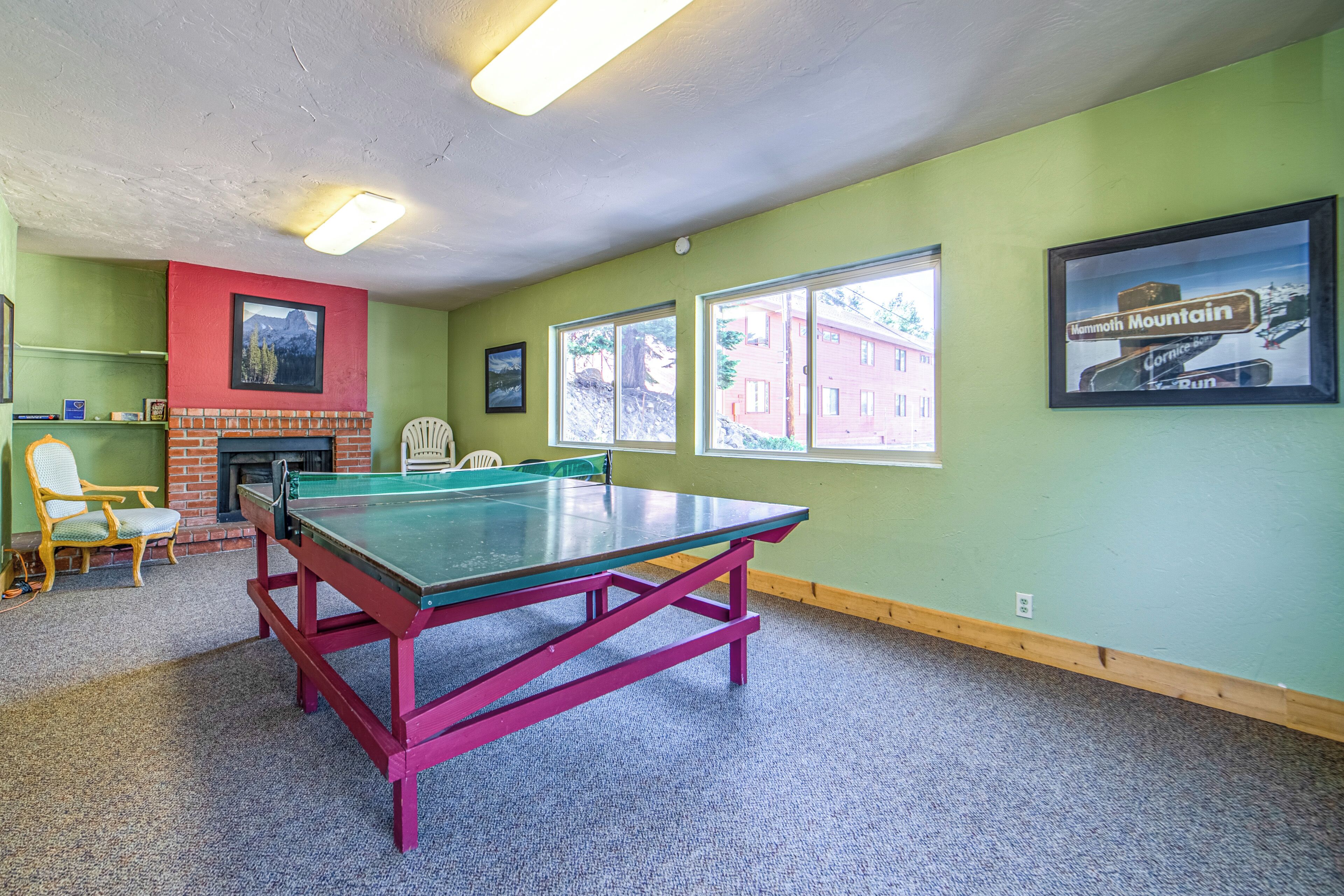 A ping pong table in a room with green walls, a fireplace, and a framed picture of a mountain.