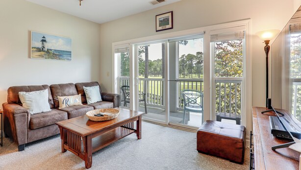 A living room with a brown leather sofa, a wooden coffee table, and a sliding glass door leading to a balcony. - ~ 6 Mi to Ocean w/ Pool & Golf: Myrtle Beach Condo (Myrtle Beach)