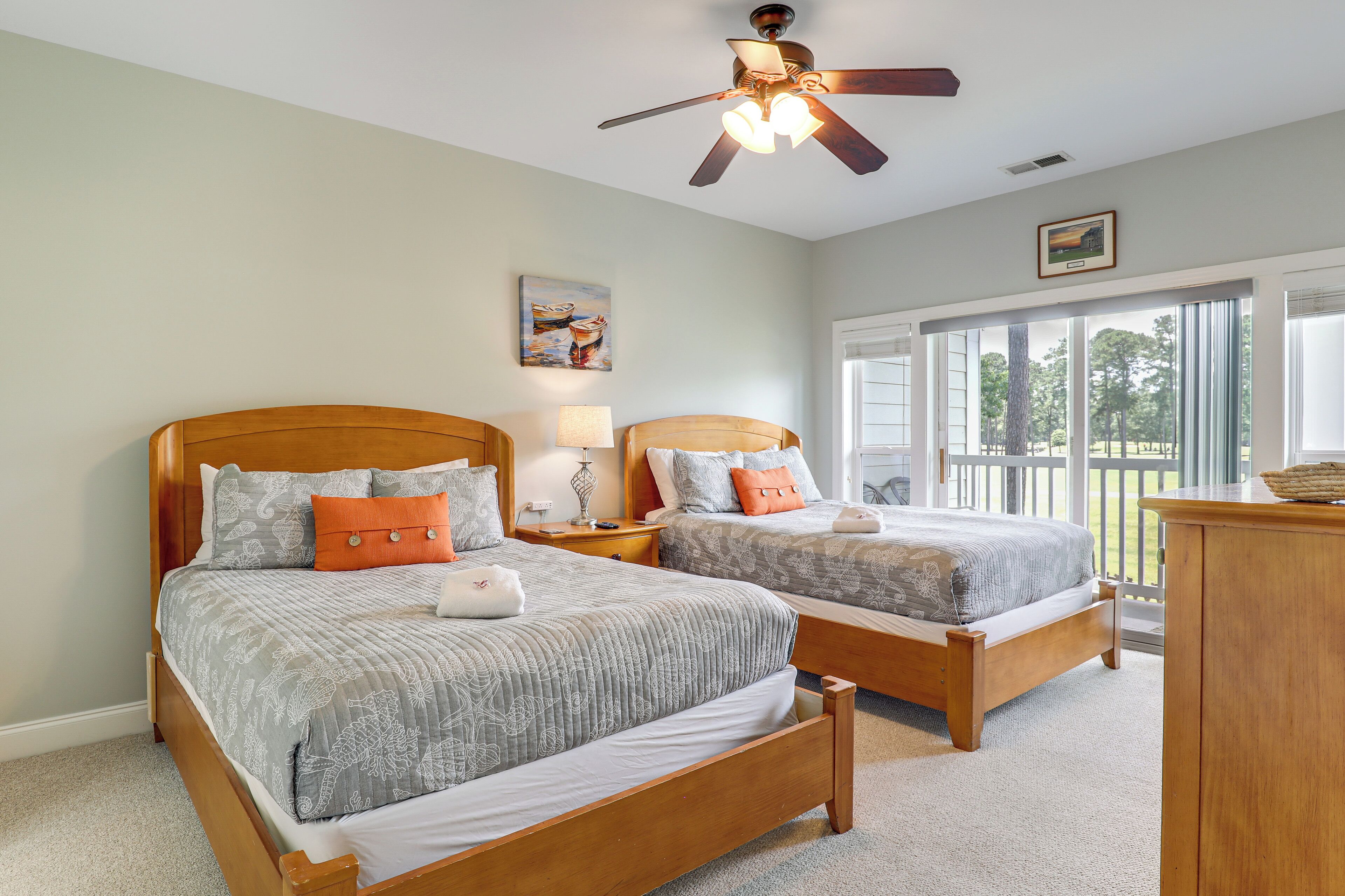 A bedroom with two wooden beds, a ceiling fan, a large window with a view of trees, and a wooden dresser.