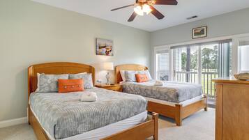 A bedroom with two wooden beds, a ceiling fan, a large window with a view of trees, and a wooden dresser.