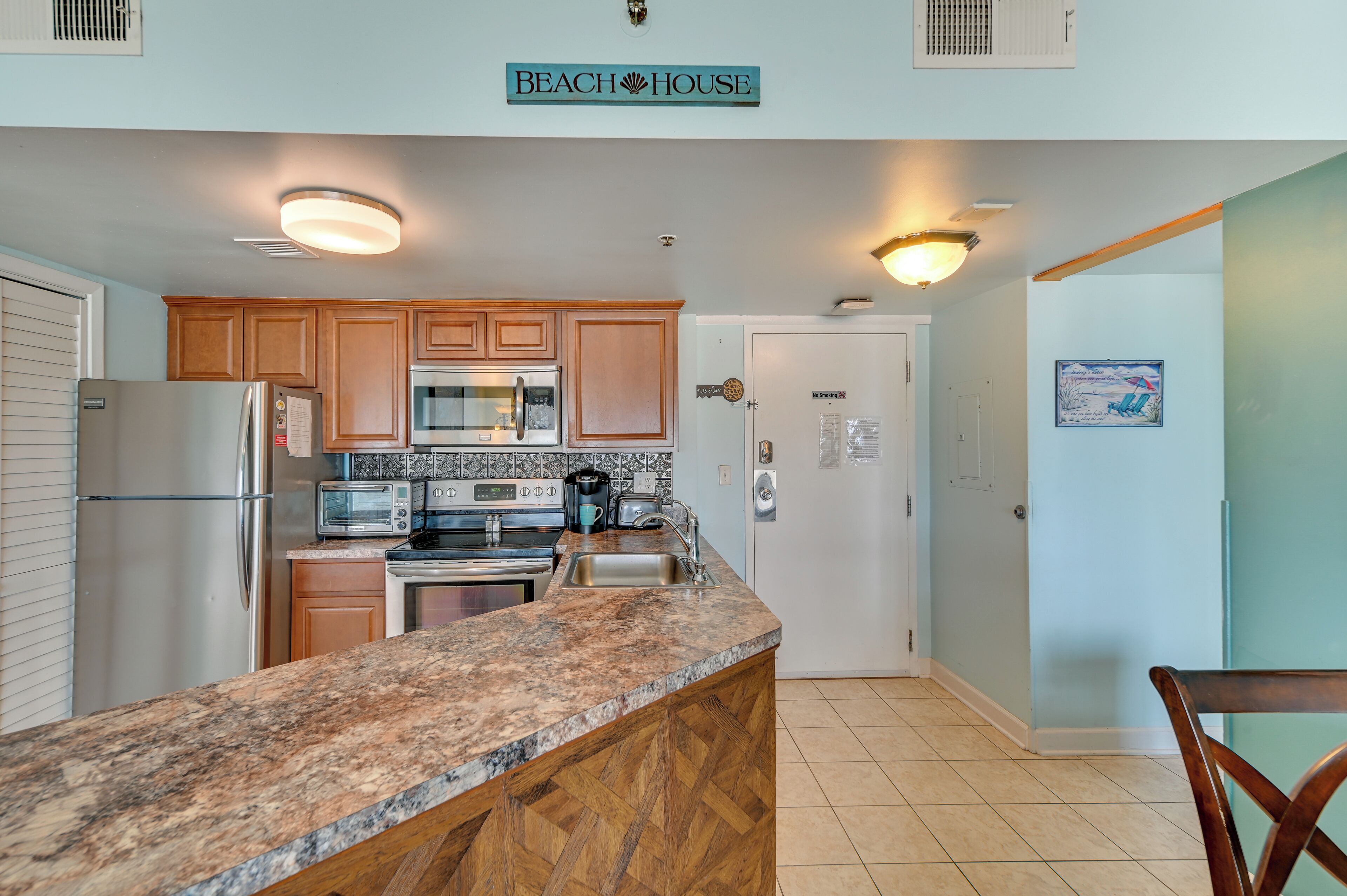 A kitchen with wooden cabinets, granite countertops, stainless steel appliances, and a sign reading 'Beach House'.
