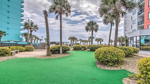A well-maintained green lawn with palm trees and bushes, surrounded by modern buildings. - Pool Access: Oceanfront Myrtle Beach Getaway! (Myrtle Beach)