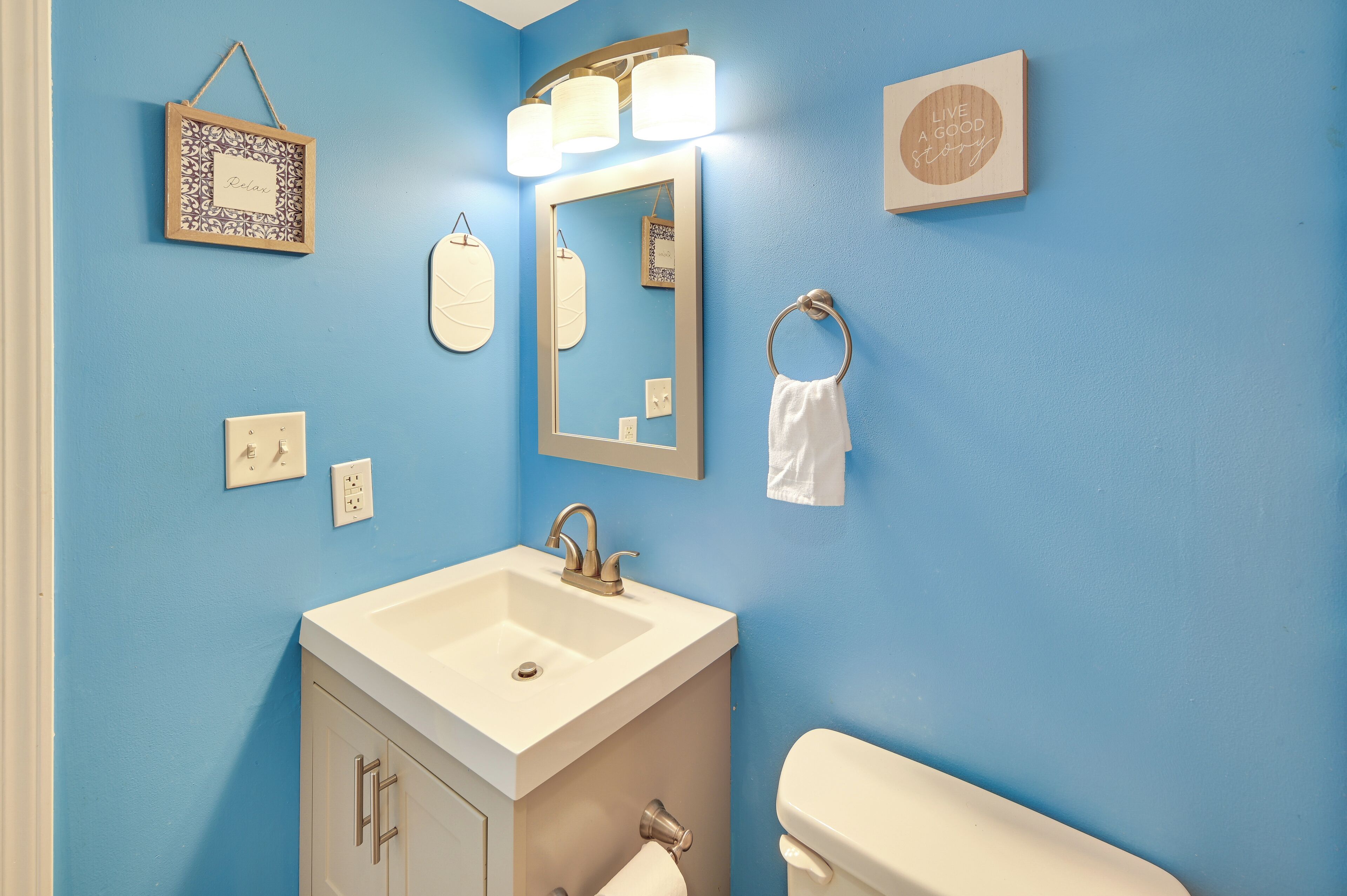 A bathroom with a blue wall, a white sink, a mirror, a towel ring, and a toilet.