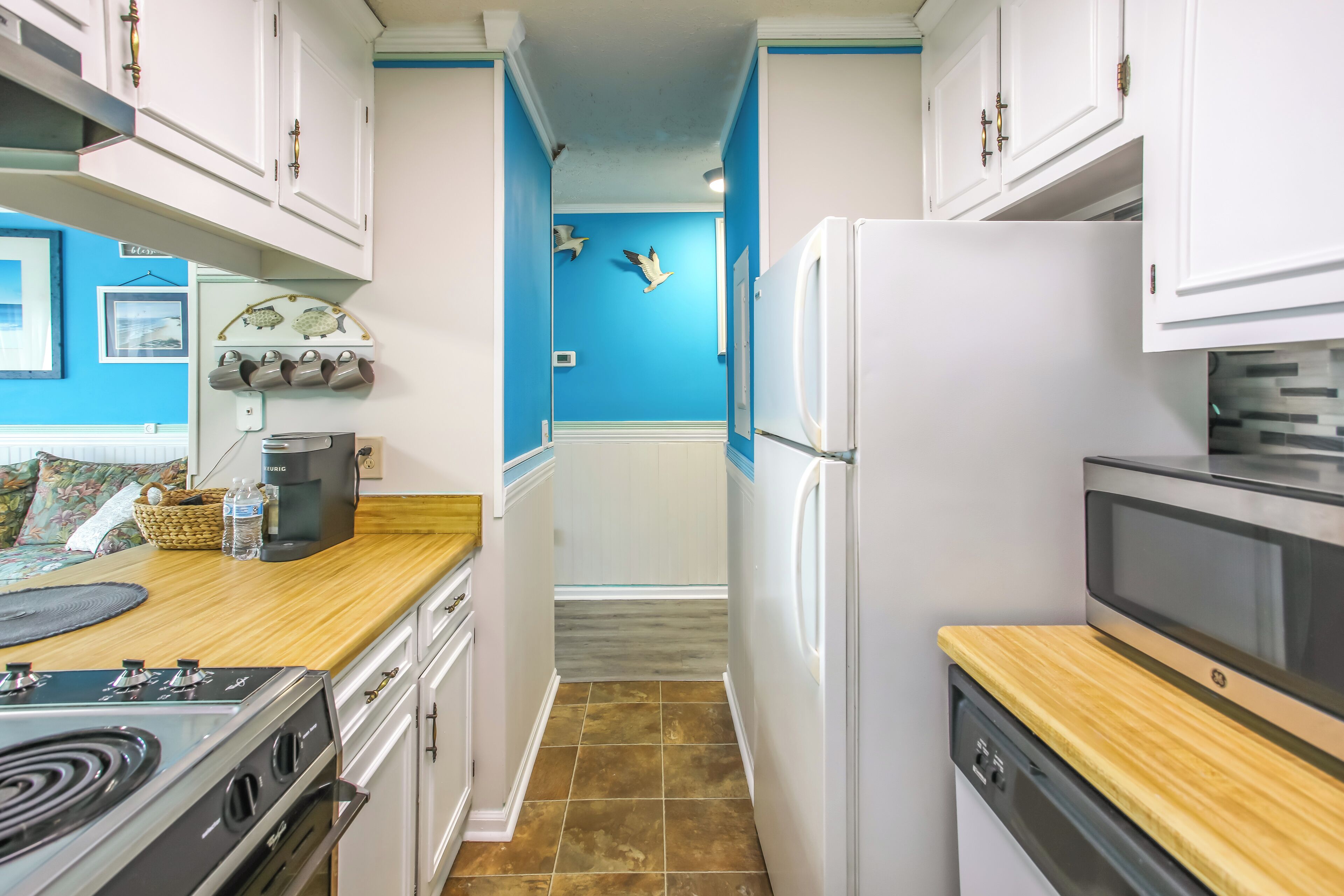 A narrow kitchen with white cabinets, a wooden countertop, a stove, a refrigerator, and a microwave.