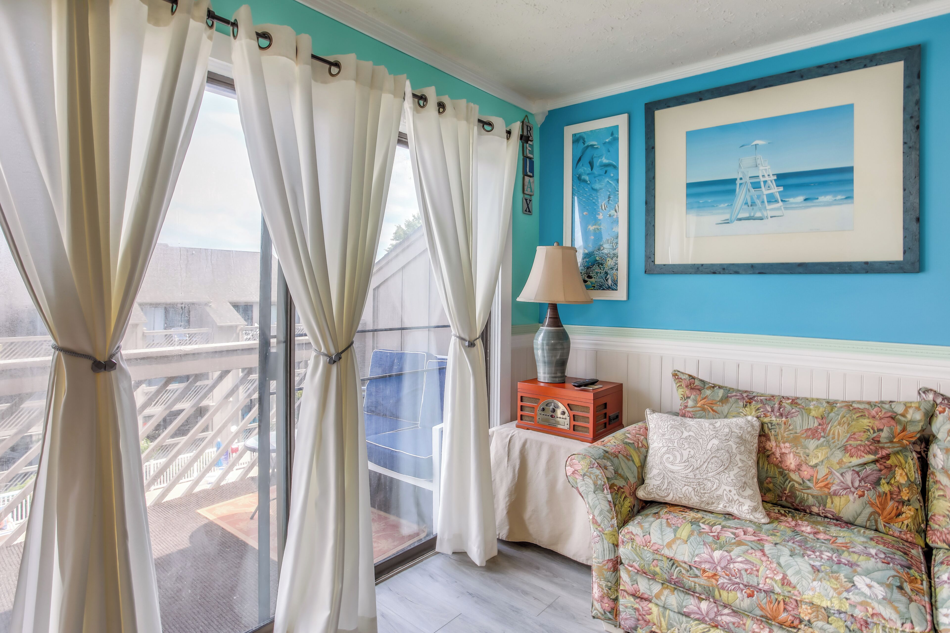 A room with a view of a balcony, a sofa with floral upholstery, and a framed picture on the wall.