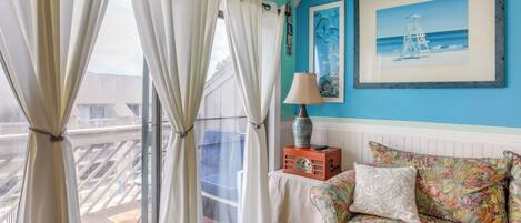 A room with a view of a balcony, a sofa with floral upholstery, and a framed picture on the wall.