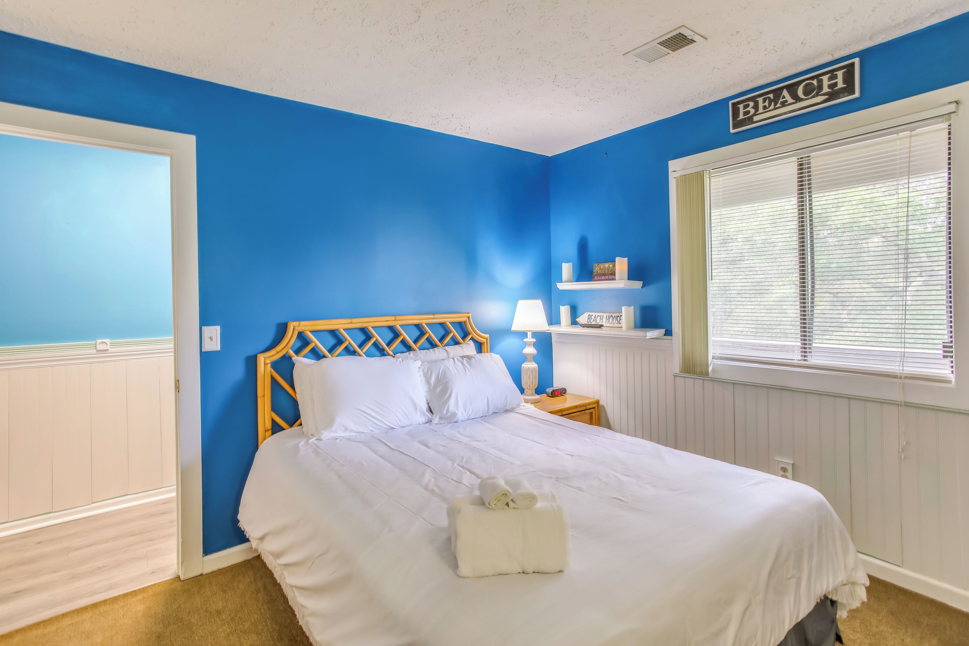 A bedroom with a blue wall, a wooden headboard, a white bedspread, and a sign that reads "BEACH".