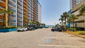 A multi-story hotel with balconies, parked cars, and palm trees along the street. - Myrtle Beach Studio w/ Pools, Walk to Beach! (Myrtle Beach)
