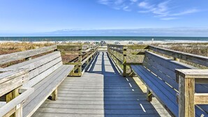 Une promenade en bois menant à une plage, avec des bancs et des parasols.