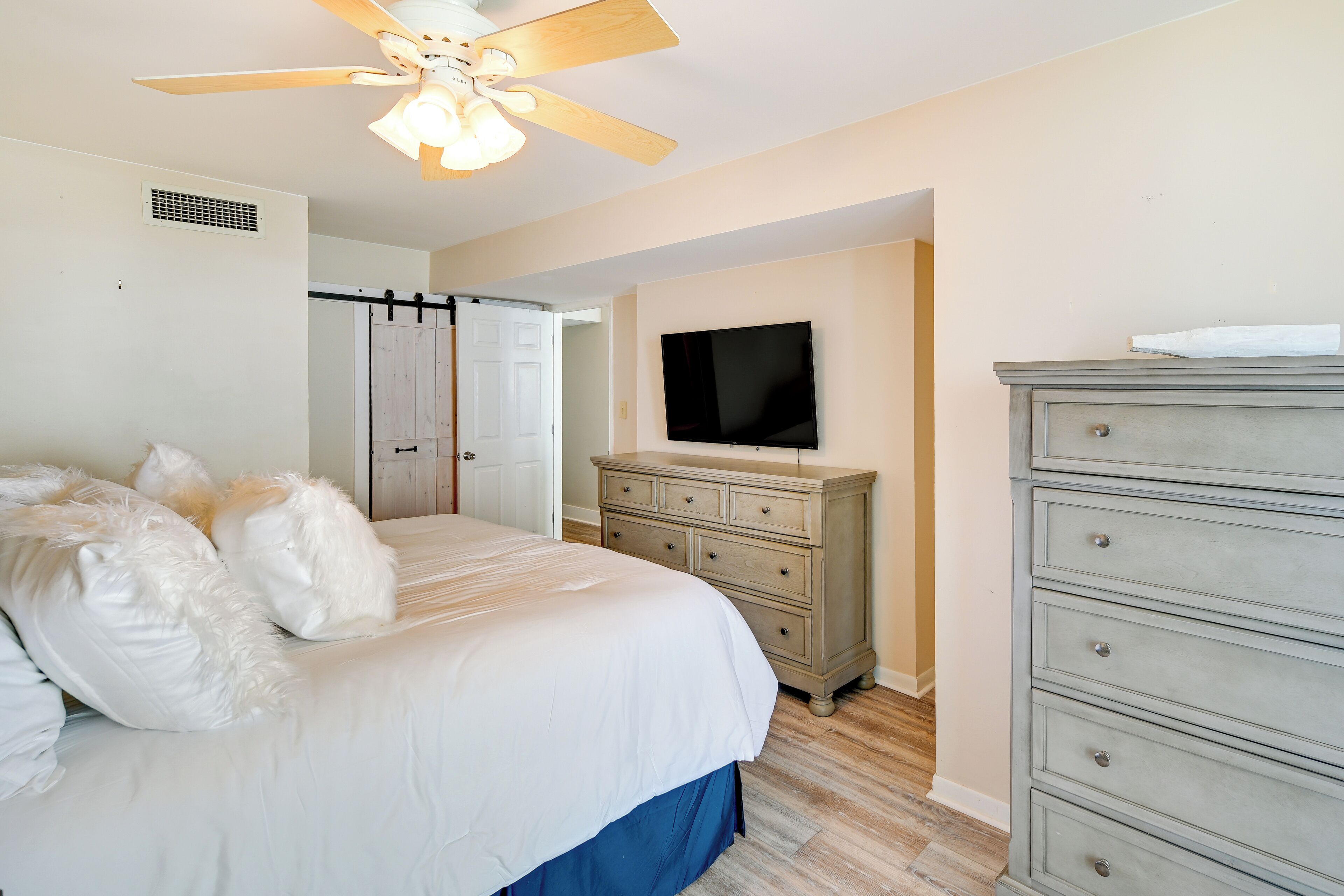 Un dormitorio con cama, cómoda, televisor y ventilador de techo.