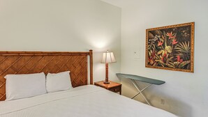 Een opgemaakt bed met een houten hoofdbord, een bedlampje en een tafeltje met een groene blad.