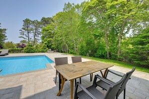 A backyard with a swimming pool, a wooden table, and wicker chairs.