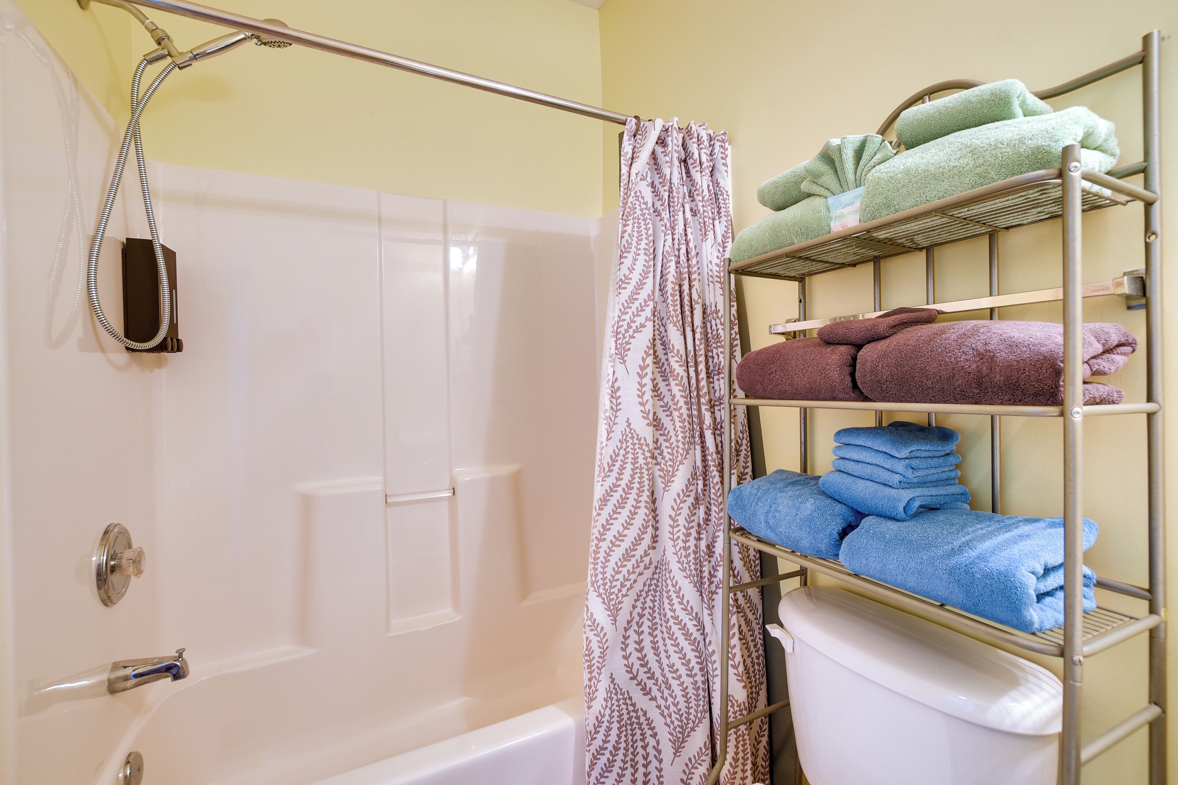 Un baño con ducha, inodoro y un perchero con toallas dobladas.