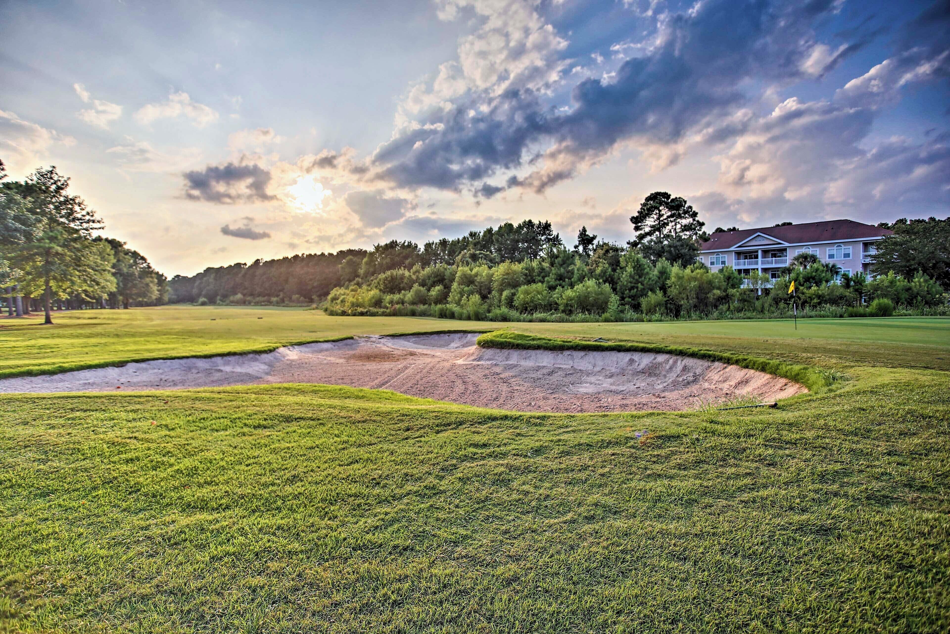 Un parcours de golf avec un bunker de sable, une pelouse verdoyante et un bâtiment en arrière-plan.