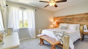 Un dormitorio con cabecera de madera, cama con ropa blanca, mesita de noche con lámpara y ventana con cortinas.