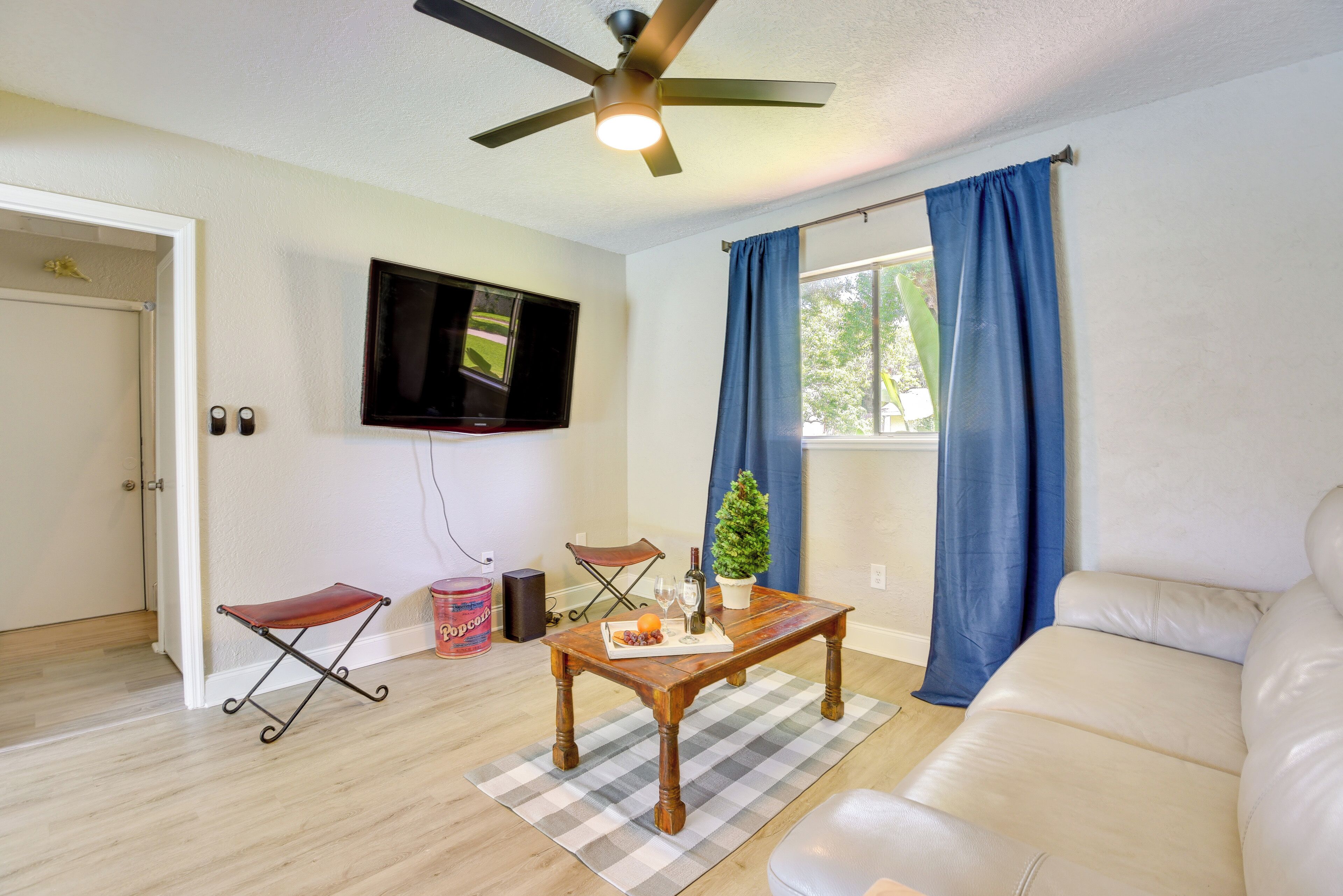 A living room with a wooden coffee table, a television mounted on the wall, a blue curtain, and a beige sofa.