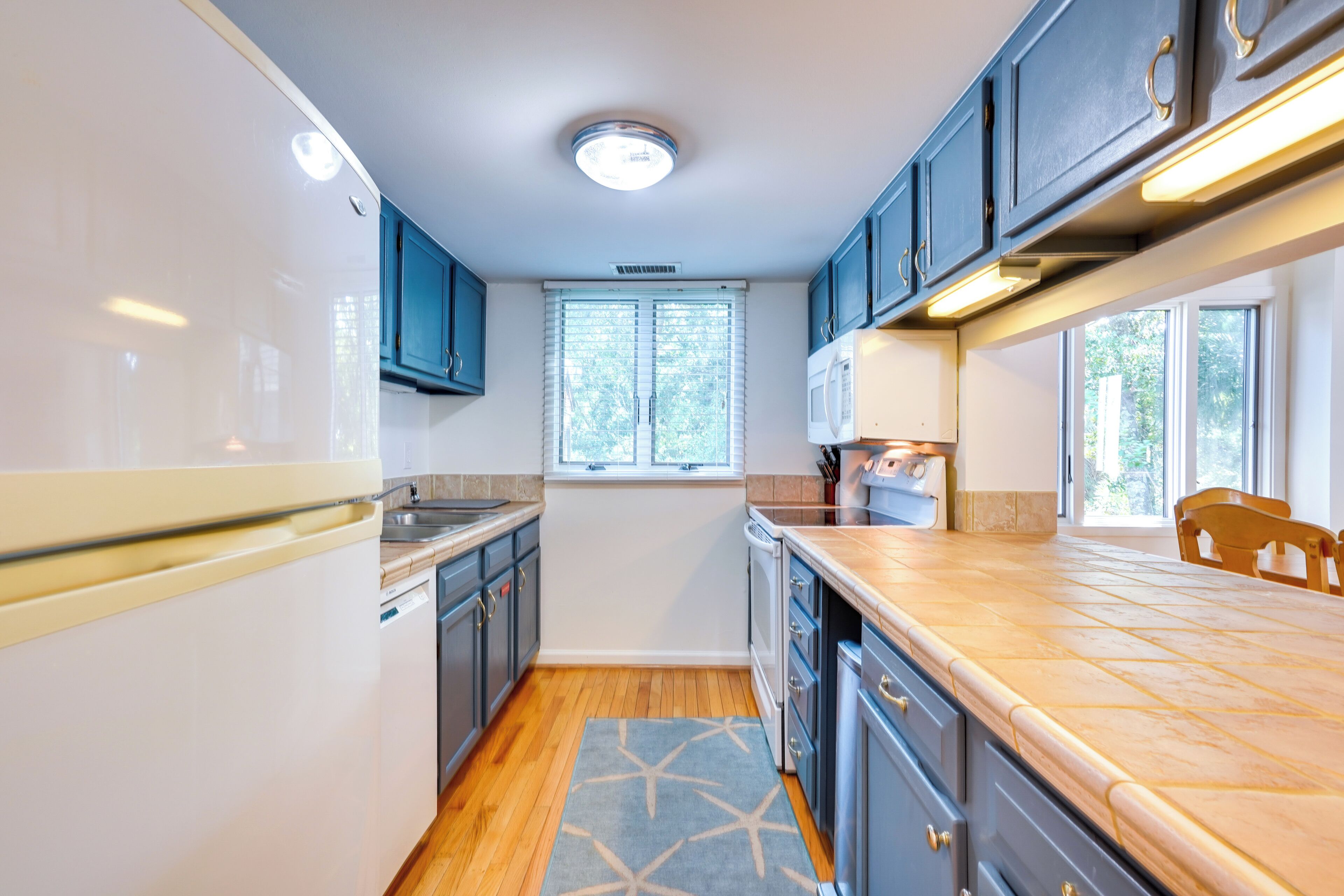 A modern kitchen with white cabinets, a wooden countertop, and a window with blinds.
