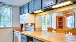 A kitchen with dark cabinets, a large island, a microwave, and a chandelier. - Kiawah Island Vacation Rental: Walk to Beach! (Kiawah Island)