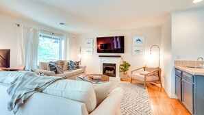 A modern living room with a sofa, coffee table, and a TV mounted above a fireplace. - Kiawah Island Vacation Rental: Walk to Beach! (Kiawah Island)