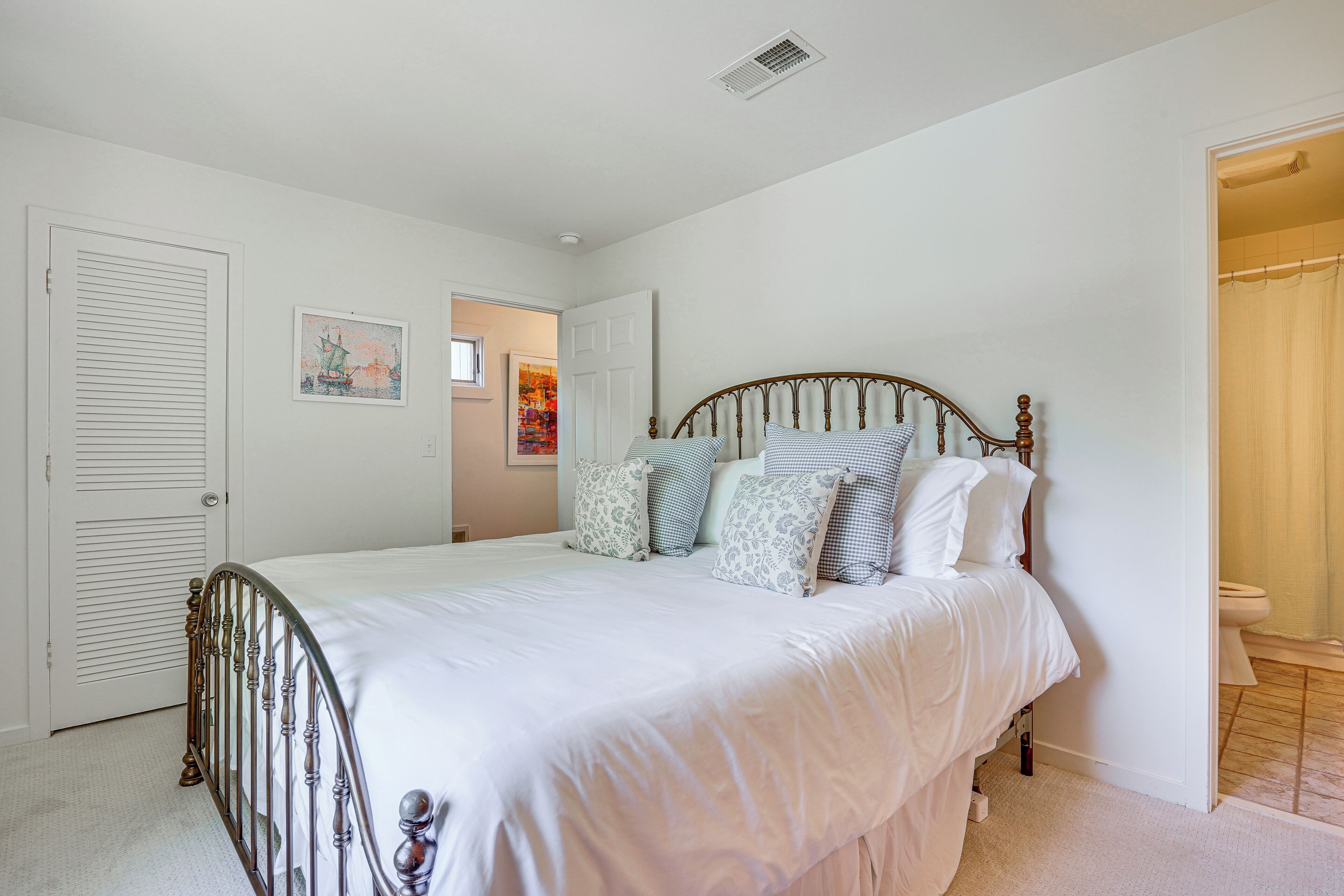 A bedroom with a bed, white walls, a door, and a bathroom visible through an open door.