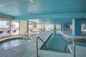 Une piscine intérieure avec des parois en verre transparent, un plafond bleu et un sol carrelé.