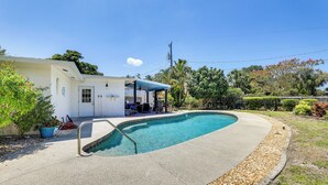 A swimming pool with a covered patio area, surrounded by a well-maintained garden and a white building. - Bradenton Retreat Near Beaches w/ BBQ & Fire Pit (Bradenton)